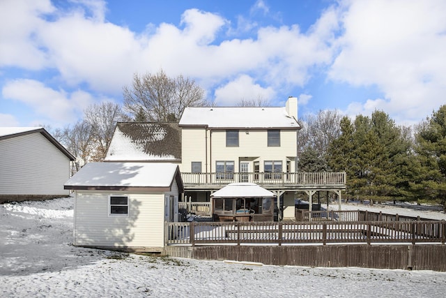 snow covered back of property with a wooden deck and a shed