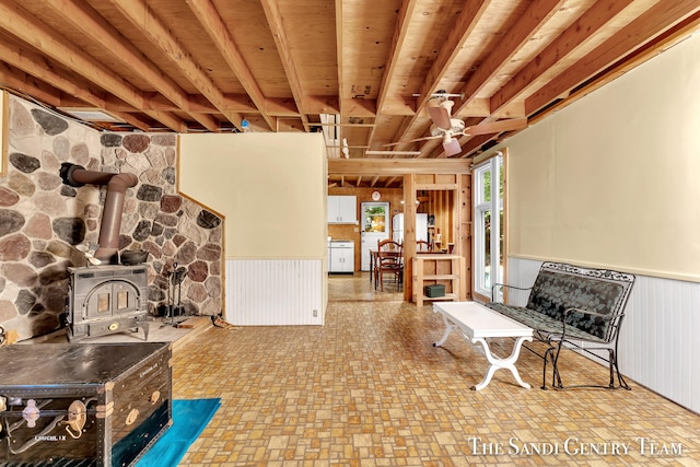 basement featuring light tile patterned flooring, wood ceiling, a wood stove, and ceiling fan