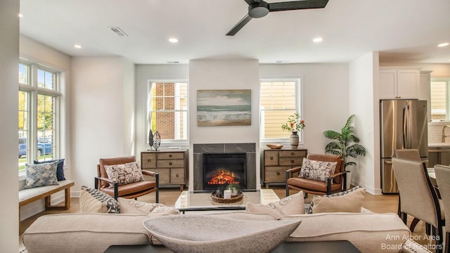 living room featuring ceiling fan, light hardwood / wood-style flooring, and a tile fireplace