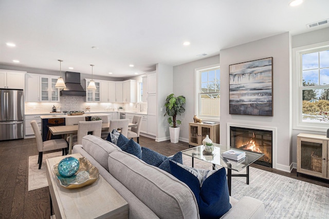 living area with dark wood-style floors, plenty of natural light, a glass covered fireplace, and visible vents