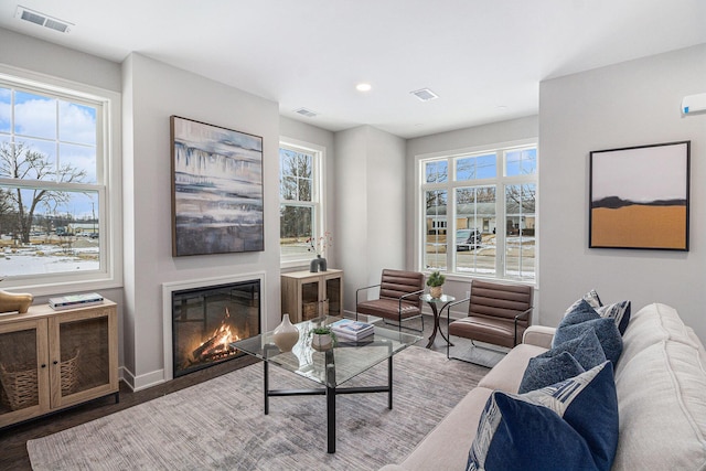 living area featuring a glass covered fireplace, visible vents, baseboards, and wood finished floors