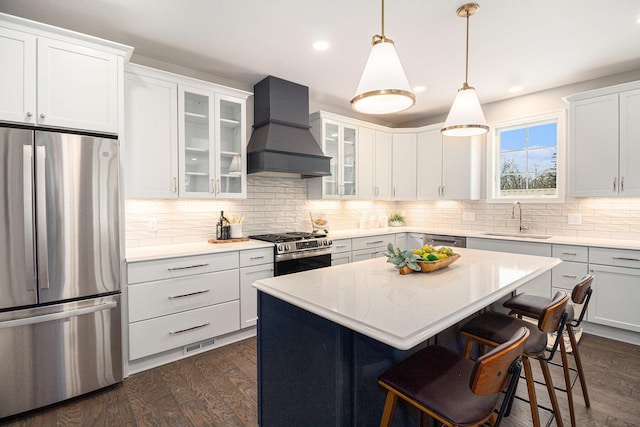 kitchen with dark wood finished floors, custom range hood, appliances with stainless steel finishes, a kitchen bar, and a sink