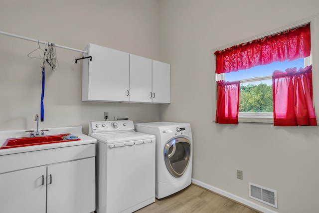 laundry area featuring sink, washer and dryer, light hardwood / wood-style floors, and cabinets