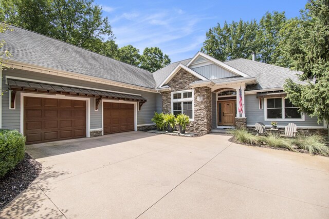 craftsman-style home featuring an attached garage, stone siding, a shingled roof, and concrete driveway