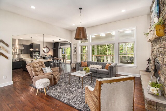 living room with dark hardwood / wood-style flooring, a healthy amount of sunlight, and a stone fireplace