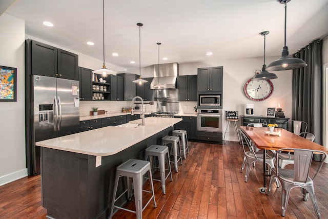 kitchen featuring wall chimney range hood, tasteful backsplash, appliances with stainless steel finishes, and dark hardwood / wood-style flooring