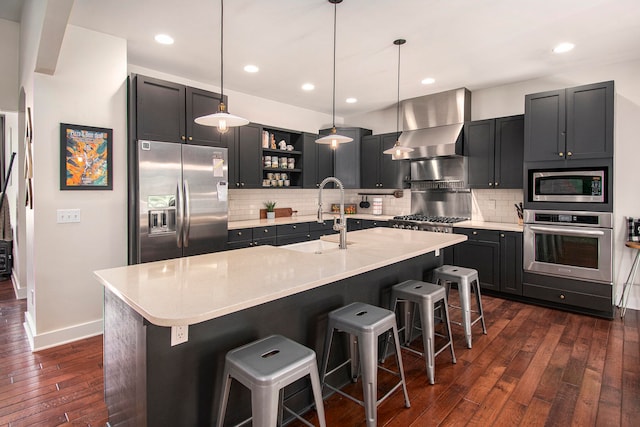 kitchen featuring a kitchen breakfast bar, sink, dark hardwood / wood-style flooring, appliances with stainless steel finishes, and wall chimney range hood