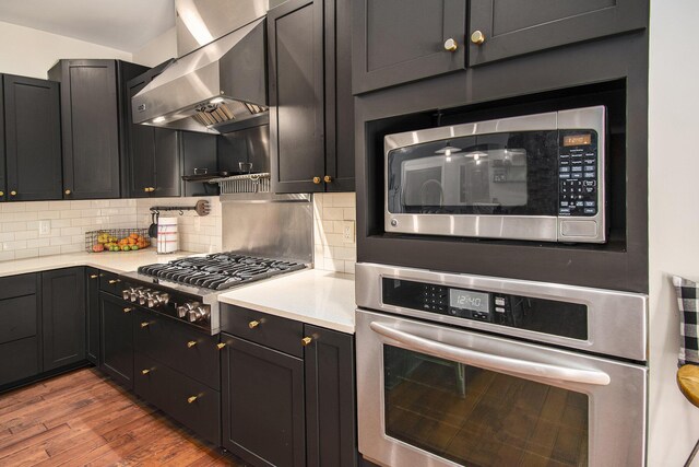 kitchen with hardwood / wood-style floors, appliances with stainless steel finishes, decorative backsplash, and wall chimney range hood