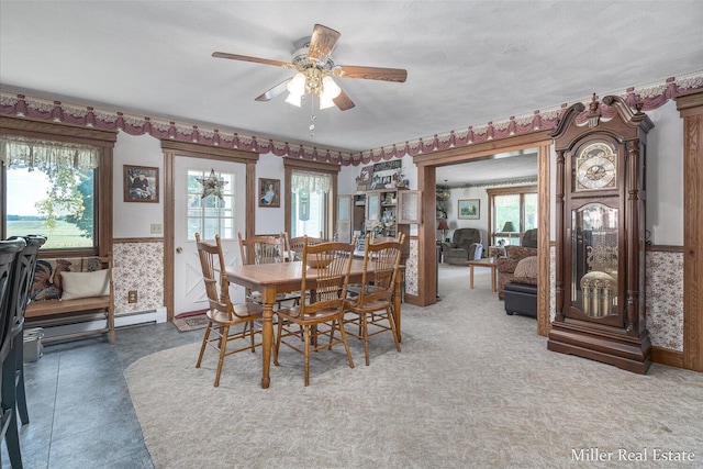 dining room featuring a wainscoted wall, a baseboard heating unit, a ceiling fan, and wallpapered walls