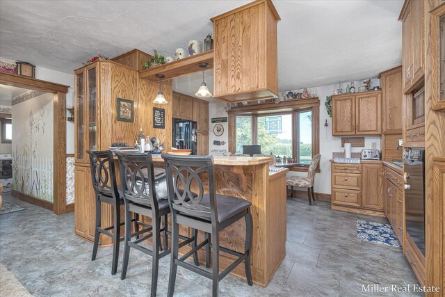 kitchen featuring a breakfast bar, stone finish floor, black fridge with ice dispenser, brown cabinetry, and light countertops