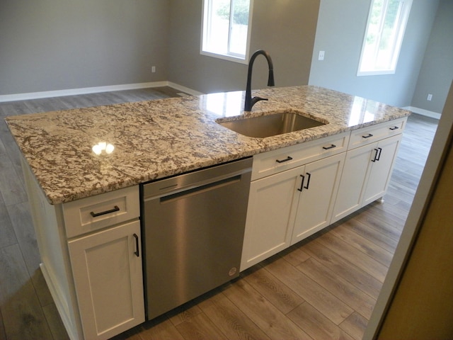 kitchen featuring light stone counters, stainless steel dishwasher, sink, white cabinetry, and an island with sink