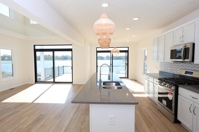 kitchen featuring a center island with sink, sink, white cabinetry, decorative light fixtures, and stainless steel appliances