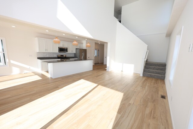 kitchen with white cabinets, light hardwood / wood-style floors, stainless steel appliances, and decorative light fixtures