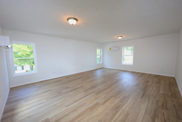 empty room with light wood-type flooring, a wall mounted air conditioner, and a healthy amount of sunlight