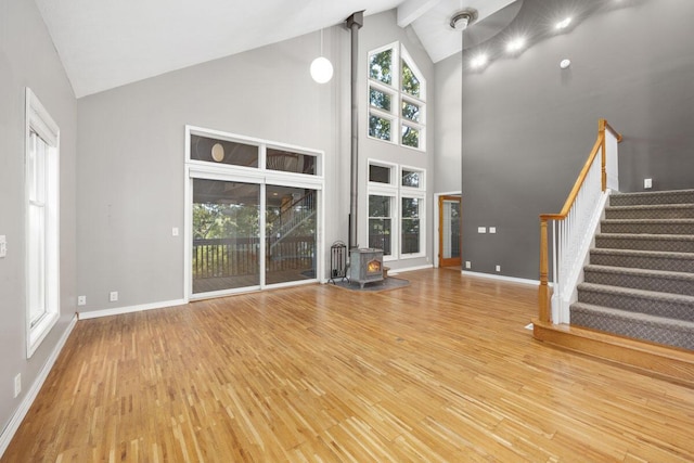 unfurnished living room featuring high vaulted ceiling, a wood stove, and wood-type flooring