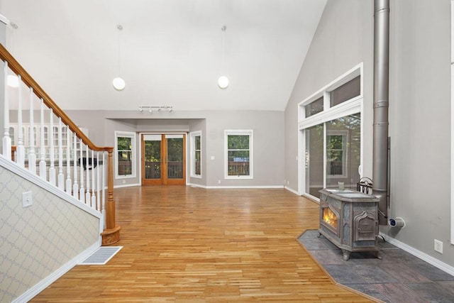 foyer entrance featuring high vaulted ceiling, a wood stove, french doors, and light wood-type flooring