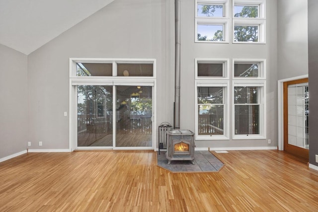 unfurnished living room with a wood stove, hardwood / wood-style floors, and high vaulted ceiling