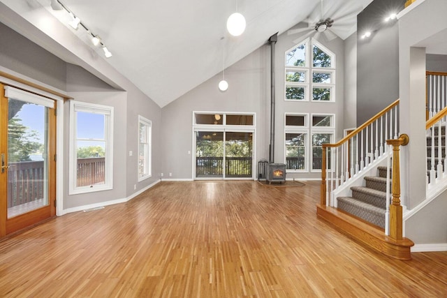 unfurnished living room with track lighting, wood-type flooring, ceiling fan, high vaulted ceiling, and a wood stove