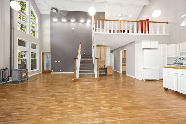 unfurnished living room featuring beamed ceiling, a wood stove, light hardwood / wood-style floors, ceiling fan, and high vaulted ceiling