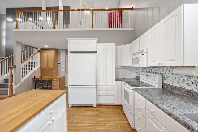 kitchen featuring white cabinetry, light hardwood / wood-style flooring, a high ceiling, white appliances, and tasteful backsplash