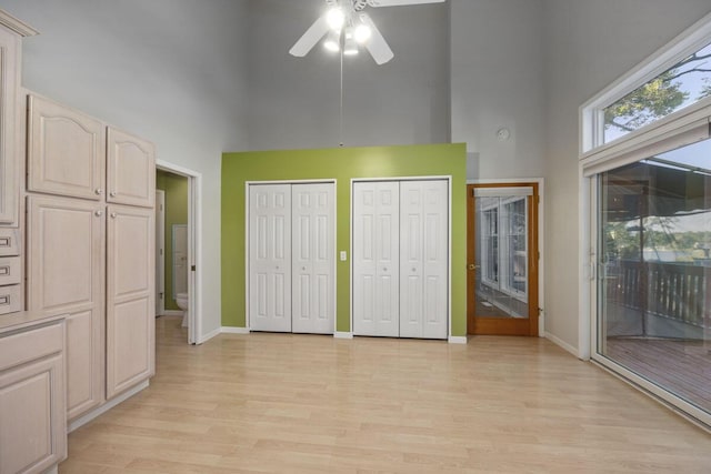 unfurnished bedroom featuring a towering ceiling, access to outside, light hardwood / wood-style floors, and multiple closets