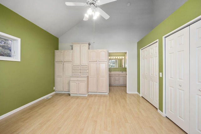 unfurnished bedroom with lofted ceiling, light wood-type flooring, ceiling fan, connected bathroom, and two closets