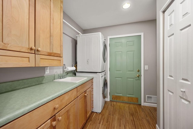 laundry room featuring sink, cabinets, stacked washer and dryer, and light hardwood / wood-style flooring