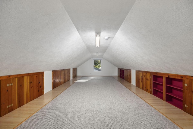 bonus room with a textured ceiling, lofted ceiling, carpet flooring, and wooden walls