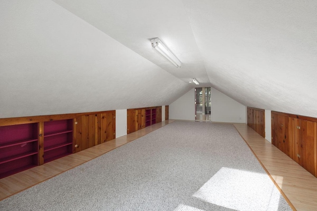 additional living space featuring built in shelves, a textured ceiling, vaulted ceiling, carpet floors, and wood walls