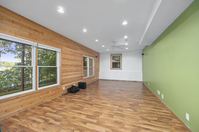 unfurnished room with light wood-type flooring, wood walls, and ceiling fan