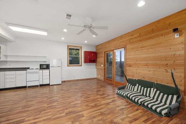 sitting room featuring ceiling fan, light wood-type flooring, a wealth of natural light, and wooden walls