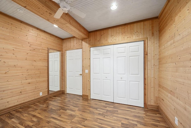 unfurnished bedroom with a closet, beamed ceiling, wood walls, and wood-type flooring