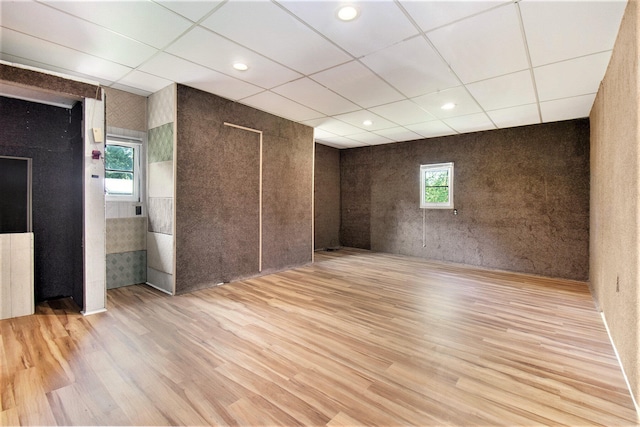 unfurnished room featuring a drop ceiling, plenty of natural light, light wood-type flooring, and tile walls