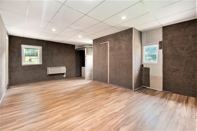 unfurnished room featuring a wealth of natural light, heating unit, wood finished floors, and a drop ceiling