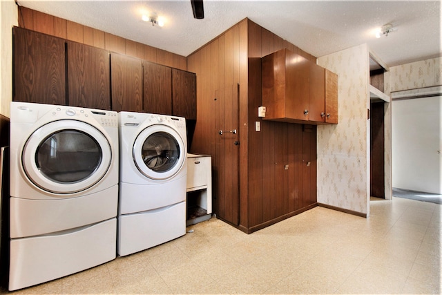 washroom featuring cabinets, a textured ceiling, wooden walls, light tile patterned floors, and independent washer and dryer