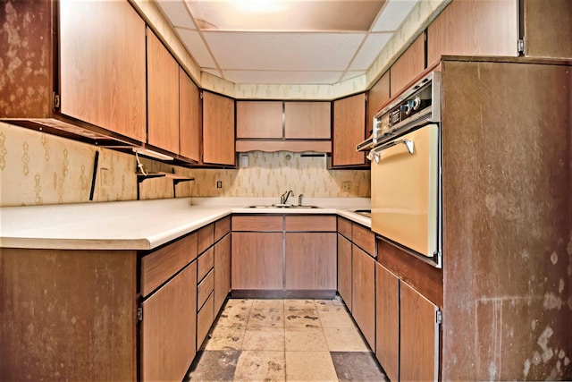 kitchen with light countertops, oven, a paneled ceiling, and a sink