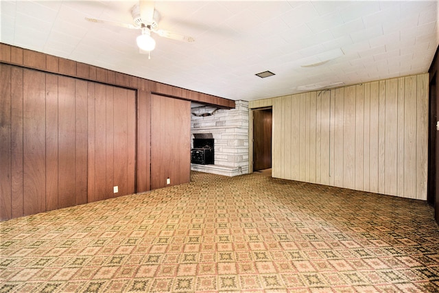 spare room featuring ceiling fan, wood walls, and a stone fireplace