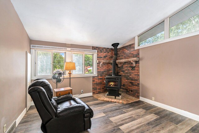 living area featuring lofted ceiling, plenty of natural light, a wood stove, and wood-type flooring