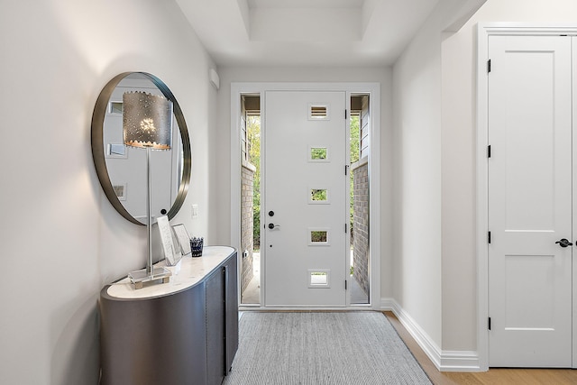 entryway featuring a raised ceiling, light wood-style flooring, and baseboards