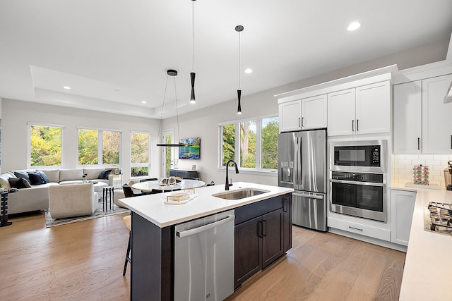 kitchen with light wood finished floors, a sink, stainless steel appliances, light countertops, and tasteful backsplash