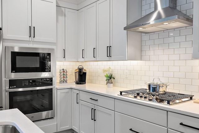 kitchen with light countertops, white cabinets, appliances with stainless steel finishes, wall chimney exhaust hood, and tasteful backsplash