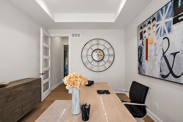 office featuring visible vents, a raised ceiling, baseboards, and wood finished floors