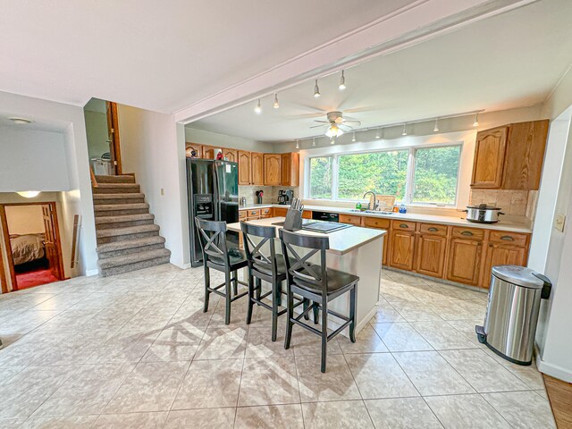 kitchen featuring sink, black fridge with ice dispenser, ceiling fan, a kitchen bar, and a kitchen island