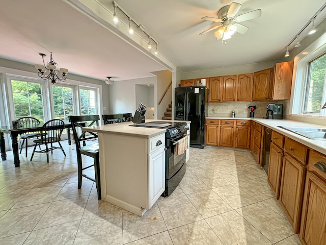 kitchen featuring light tile patterned floors, ceiling fan with notable chandelier, sink, black appliances, and a kitchen island