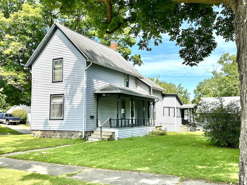 view of front of home with a front lawn, covered porch, a chimney, and a shingled roof