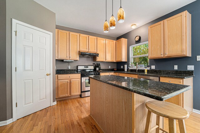 kitchen featuring light wood-type flooring, appliances with stainless steel finishes, light brown cabinetry, ventilation hood, and pendant lighting