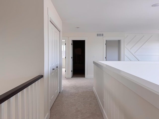 hall with light carpet, baseboards, visible vents, and an upstairs landing