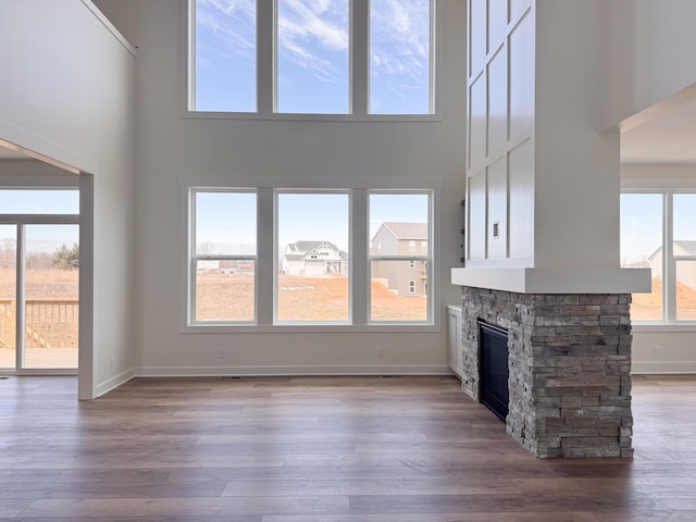 unfurnished living room with a stone fireplace, baseboards, and wood finished floors