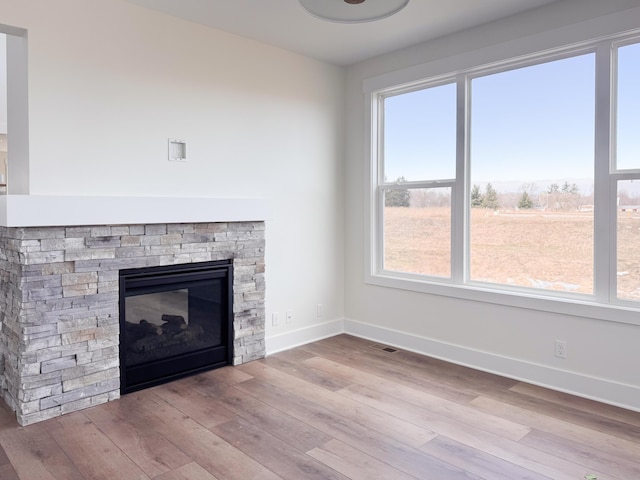 unfurnished living room featuring baseboards, visible vents, wood finished floors, and a stone fireplace