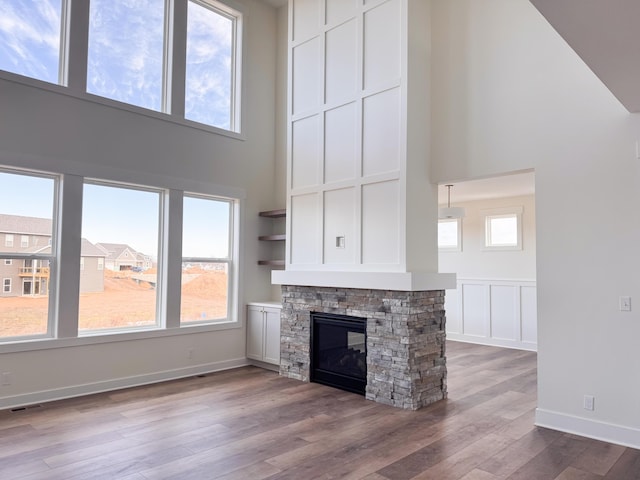 unfurnished living room featuring visible vents, a decorative wall, a towering ceiling, a stone fireplace, and wood finished floors